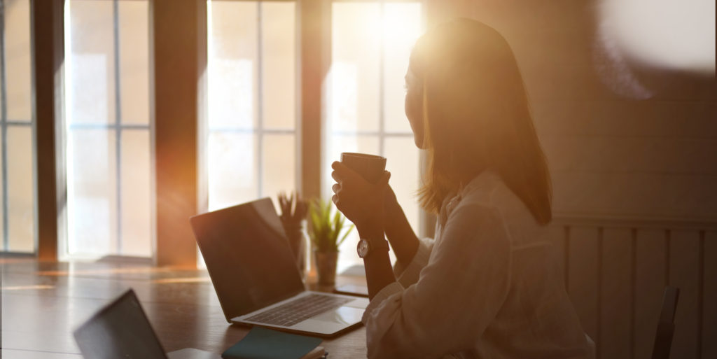 A kép az online végzett tartalommarketing és tartalomgyártás tanácsadás előnyeit szimbolizálja - a hölgy laptopja előtt ülve kényelmesen kávét szürcsöl.