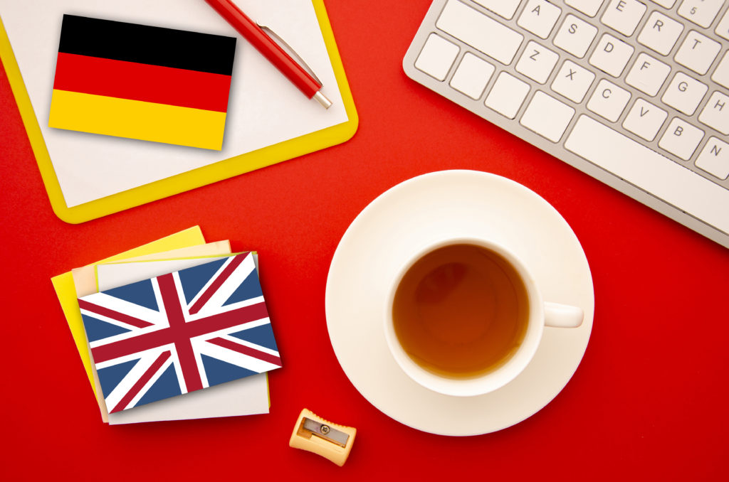 A képen egy csésze kávé, valamint egy német és egy angol zászló látható, az angol magyar és a német magyar fordítást szimbolizálva.